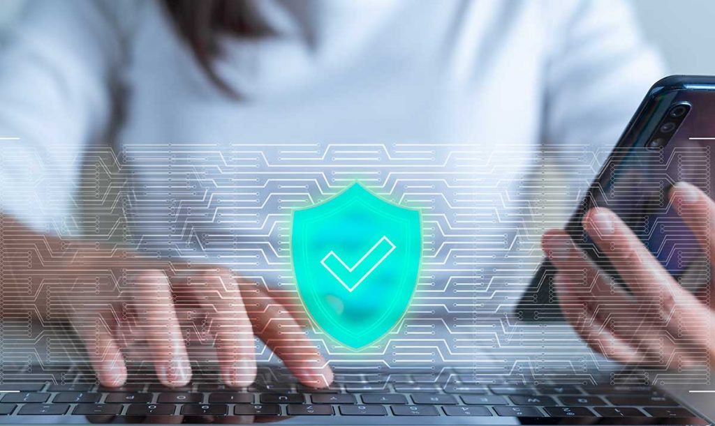 Donna digita sulla tastiera di un computer mentre regge il cellulare con l'altra mano