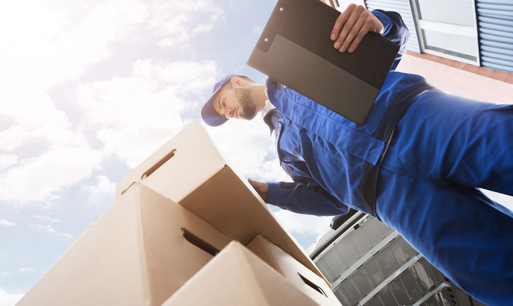 Corriere, in piedi vicino ad una pila di scatole, tiene in mano una cartellina con i Documenti Di Trasporto (DDT)