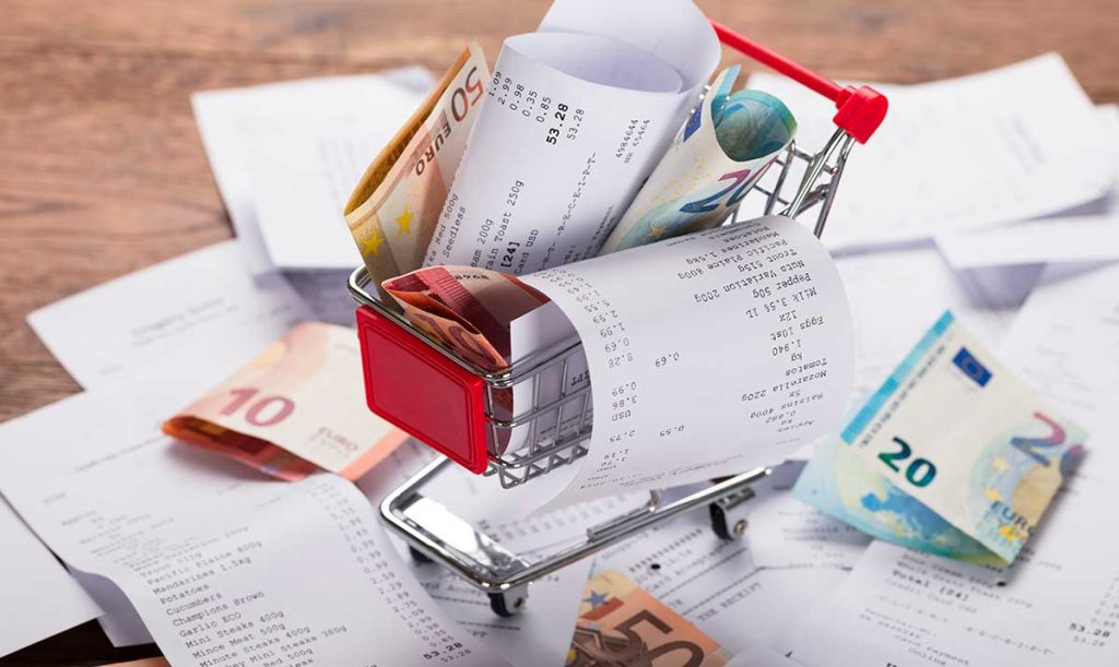 Vista dall'alto di un piccolo carrello della spesa pieno di ricevute e banconote