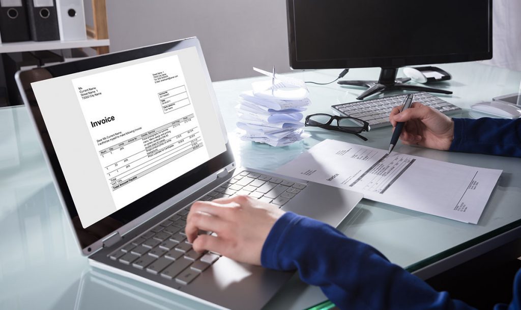 Primo piano di un uomo d'affari che lavora sul computer portatile mentre controlla una fattura cartacea