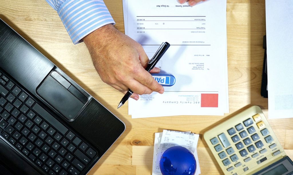 Vista dall'alto della scrivania di un contabile con computer, calcolatrice e dettaglio della mano che regge una key bancaria per pagare le fatture