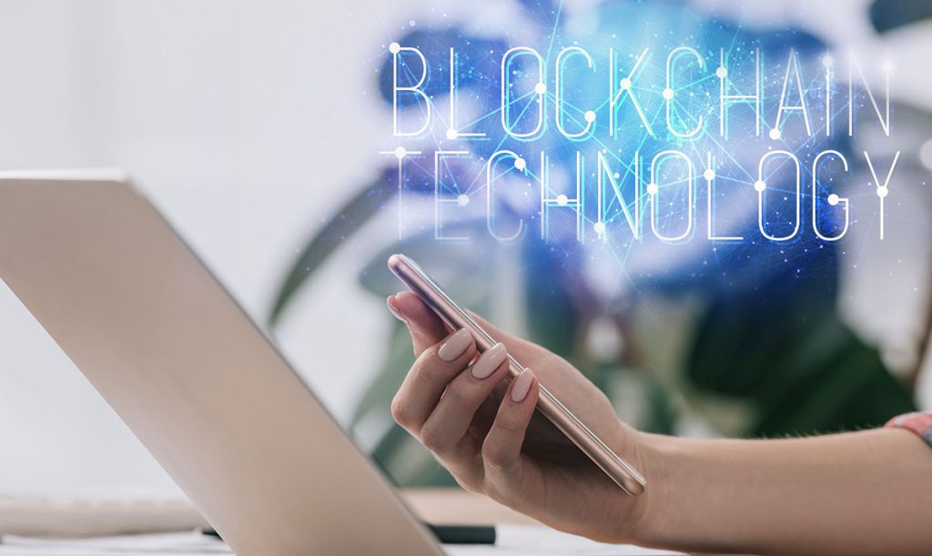 Primo piano di una mano femminile che regge un cellulare davanti ad un computer portatile