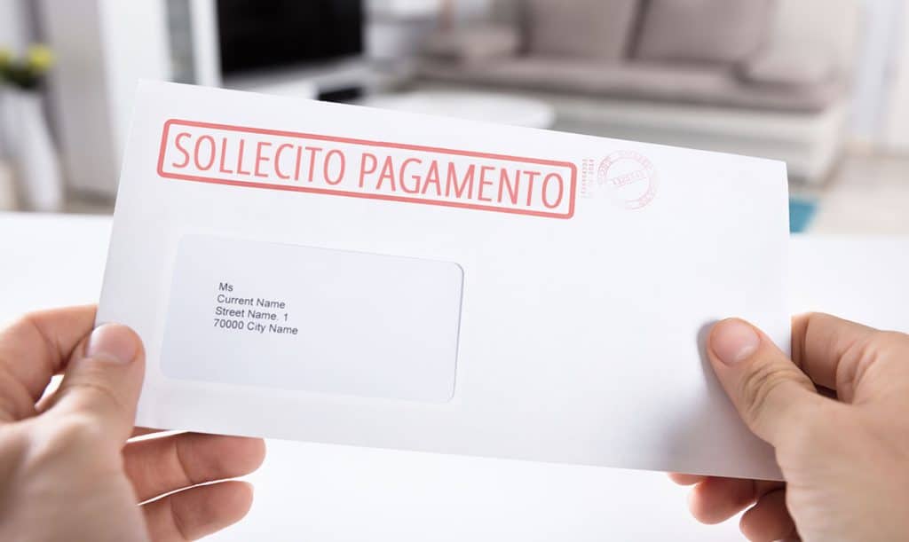 Primo piano delle mani di una persona che tiene una busta delle lettere con un sollecito di pagamento di una fattura