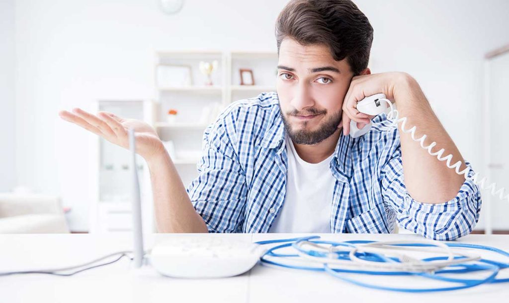 Giovane uomo con modem, fili e cornetta di un telefono in mano, in difficoltà per la mancanza di rete internet