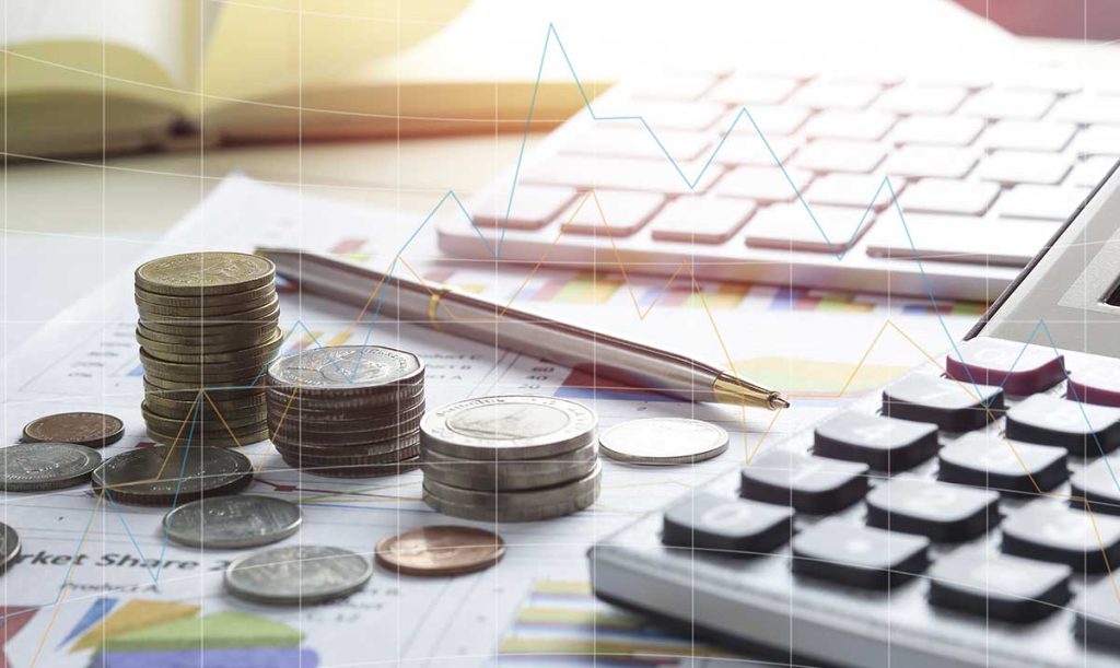 Pile di monete, fogli con grafici statistici, calcolatrice e tastiera di un pc.