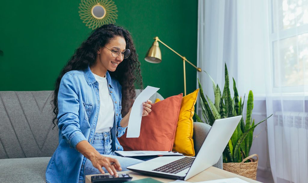 Giovane donna d'affari con calcolatrice e laptop che consulta lavora a casa.