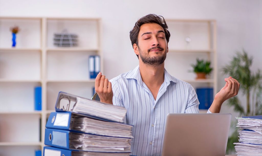 Uomo in posizione zen alla scrivania con pc e raccoglitori di documenti