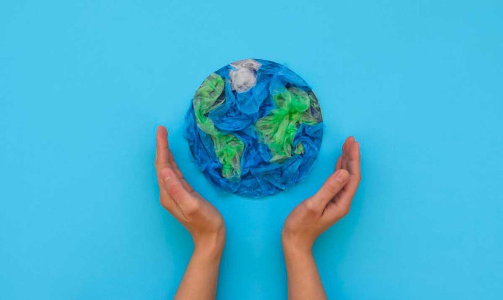 Concetto di sostenibilità: mani che racchiudono dei sacchetti di plastica blu e verdi che creano la forma di un globo terrestre