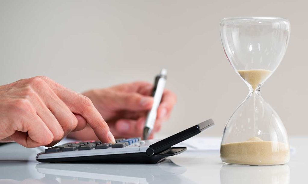 Primo piano di una clessidra di fronte alla mano dell'imprenditore che calcola le sanzioni previste in caso di fattura tardiva
