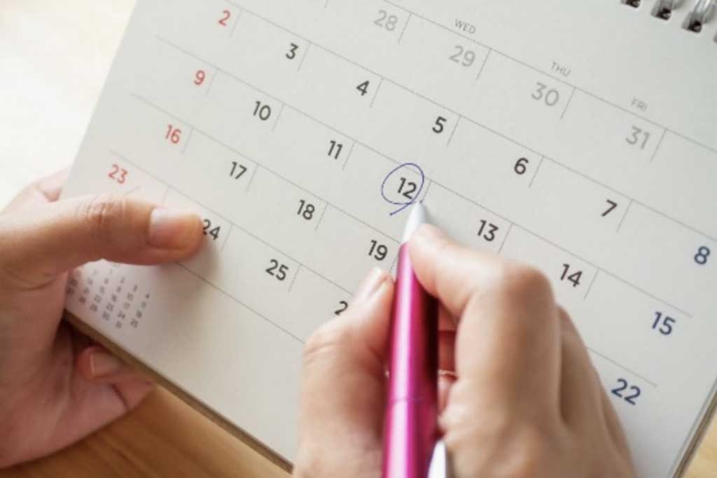 Mani che prendono appunti delle scadenze degli obblighi del regime forfettario su un calendario