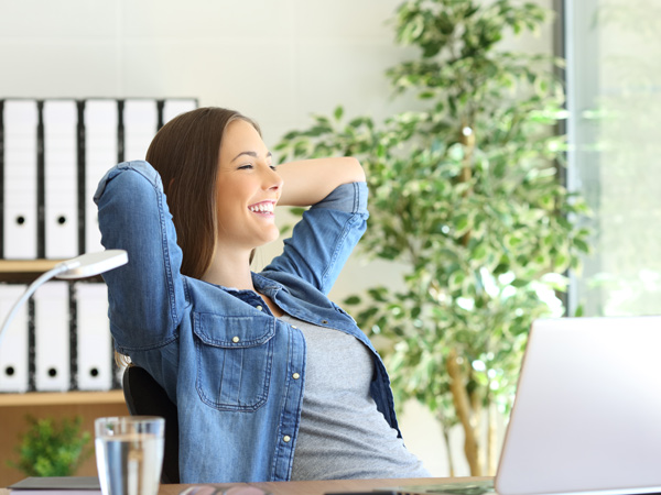 Donna d'affari soddisfatta con le braccia sulla testa che ride seduta alla scrivania del suo ufficio